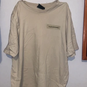 Beige Peak Performance t-shirt - Snygg beige t-shirt från Peak Performance med klassisk logga på bröstet. T-shirten har rund halsringning och korta ärmar. Tillverkad i mjuk bomull som känns skön mot huden. Perfekt för en clean och avslappnad stil.