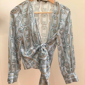 Somrig Silky Blus/ Skjorta med Knut i Midjan - Denna himmelsblå topp med knutdetalj i midjan är en av mina absoluta favoriter. Den silkeslena känslan och de uppvikta ärmarna ger ett elegant men avslappnat intryck. Jag älskar hur mångsidig den är – perfekt att klä ner för en kvällsdrink eller bära till jobbet för en mer uppklädd look. 