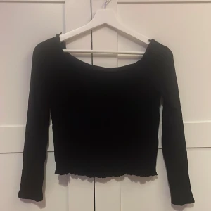 Svart långärmad topp Gina Tricot - Svart långärmad topp från Gina Tricot med croppad passform och lätt rynkad, vågig nederkant. Tunn och stretchig, perfekt att styla med jeans eller kjol. Enkel och stilren design med rundad halsringning. Ärmlängd 54 cm, 34 cm i längden. 