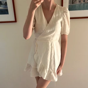 Omlottklänning från & Other Stories - Vit kort omlottklänning från & Other Stories i linne. Klänningen har puffiga korta ärmar, v-ringning och volangkant nertill.