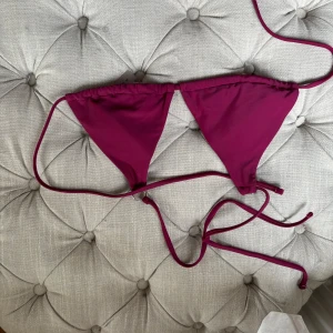 Mörkrosa trekantsbikini med knyt - Snygg trekantsbikini i mörkrosa med tunna knytband både i nacken och runt ryggen. Bikinin har en klassisk triangelmodell och är fodrad med vit insida. Perfekt för stranden eller poolen i sommar!