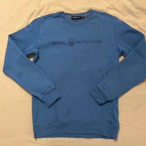 Blå Sail Racing sweatshirt M - Snygg blå sweatshirt från Sail Racing med tryckt logga på bröstet. Tröjan har rund hals, långa ärmar och är tillverkad i en mjuk bomulls- och polyestermix. Perfekt för en chill och sportig look. Lite stor i storleken.