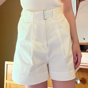 Vita högmidjade shorts med bälte - Stilrena vita shorts med hög midja och tillhörande bälte. De har breda ben, pressveck framtill och är tillverkade i ett mjukt bomullstyg. Perfekta för varma dagar när du vill ha en clean och fräsch look.