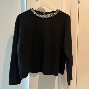 Svart stickad tröja med strass från Zara - Supersnygg svart stickad tröja från Zara med glittrande strassdetaljer runt halsringningen. Tröjan har lång ärm, rak passform och knapp i nacken. Perfekt när du vill addera lite extra bling till din outfit. Köpt för 600kr. Endast använd en gång, så i super skick! 🖤