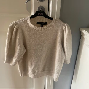 Beige stickad tröja med puffärm - Superfin beige stickad tröja från Vero Moda med korta puffärmar och rund halsringning. Tröjan har en mjuk struktur och ribbade muddar vid ärmslut och nederkant. 