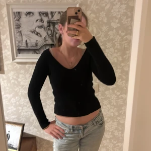 Svart v-ringad stickad tröja - Svart stickad tröja med v-ringning och lång ärm. Modellen är något croppad och har en klassisk, enkel look som passar till jeans eller kjol. 