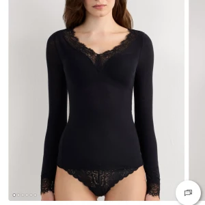 Svart långärmad topp med spetsdetaljer från intimissimi - Svart långärmad topp med snygga spetsdetaljer längs v-ringningen och vid ärmsluten. Toppens material känns mjukt och följsamt, perfekt för dig som gillar en stilren men ändå lite extra look. Passar till både jeans och kjol för en cool vibe.