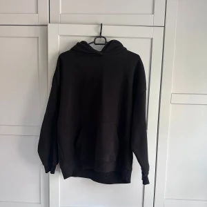Svart oversized hoodie med huva - En svart oversized hoodie med stor huva och magficka. Tröjan har långa ärmar och en avslappnad passform, perfekt för chill dagar. Enkel och stilren design som funkar till det mesta.