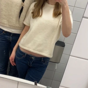 Vit stickad kortärmad tröja - Superfin vit stickad tröja med korta ärmar och rund hals. Modellen är lite croppad och har en enkel, clean look som passar perfekt till jeans. Mjuk och skön, perfekt för lager-på-lager under kyliga dagar.