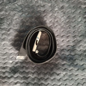 Svart tygbälte med metallspänne 110 Cm - Säljer ett svart tygbälte med klassiskt silverfärgat metallspänne. Bältet är enkelt och stilrent, perfekt för att ge en clean look till jeans eller byxor. Spännet är rektangulärt och har en smidig låsmekanism. Bältet är justerbart och passar de flesta.