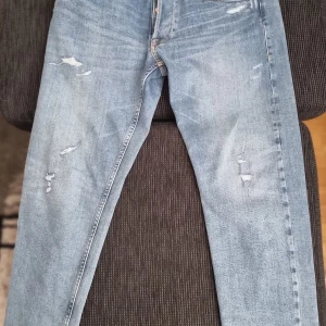 Replay ljusblå slitna jeans ronas x33,30 - Säljer ett par ljusblå jeans från Replay med snygga slitningar och broderade bakfickor. Jeansen har klassisk femficksdesign, normal passform och är tillverkade i mjukt denimtyg. Perfekta för dig som gillar en avslappnad och trendig look.
