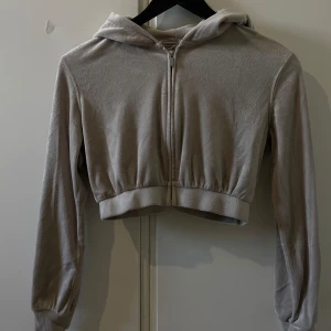 Beige croppad hoodiejacka Divided XS - Beige croppad hoodiejacka från H&M Divided i mjuk fleece. Jackan har dragkedja framtill, huva och långa ärmar. Perfekt för en chill och avslappnad stil. Passformen är normal och materialet är supermjukt mot huden.