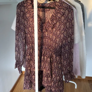 Mönstrad kortklänning från Zara - Supersöt kortklänning från Zara i lila och beige med blommigt mönster. Klänningen har långa ärmar, volangdetaljer vid halsringningen och midjan är smockad för en snygg passform. Tunt, flowigt material som känns lätt och luftigt. Inga tecken på användning, skriv för egna bilder!
