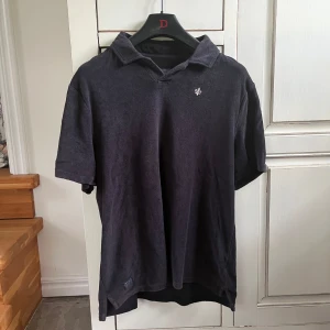 Svart pikétröja i frotté från Morris - Svart pikétröja från Morris i mjuk frotté. Klassisk krage, korta ärmar och liten broderad logga på bröstet. Perfekt för en chill och stilren look. Passar dig som gillar enkel men snygg stil.