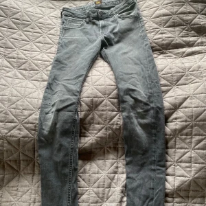 Grå skinny jeans från Lee - Säljer ett par grå jeans från Lee med klassisk femficksdesign och skinny passform. Jeansen har en snygg tvättad look, Lee-logga på bakfickan och metallknapp framtill. Perfekta för dig som gillar en smal siluett och stilren vibe.