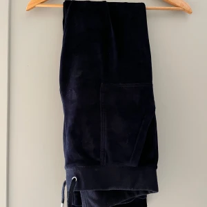 Mörkblå mjukisbyxor Juicy Couture - Mörkblå mjukisbyxor från Juicy Couture i mjuk sammet med snörning i midjan och fickor på sidorna. Perfekta för en chill och avslappnad stil. Klassisk Juicy-vibe och superbekväma.