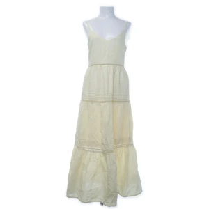 Gul långklänning med volang  - Superfin gul långklänning i bomull med tunna axelband och v-ringning. Klänningen har volanger och spetsdetaljer i midjan och längs kjolen. Justerbara axelband. Storlek 38 och i fint skick.