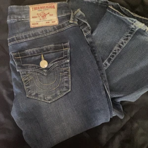 True Religion lågmidjade jeans ( pris diskuteras )  - !! Pris diskuteras !!  Säljer ett par ikoniska True Religion Joey jeans i mörkblå tvätt med kontrastsömmar och snygga fickdetaljer med silverknappar. Modellen är lågmidjad med bootcut och klassisk  stickning. Jeansen har en cool vintagekänsla . 2 och 3 bilden är ej mina men det är exact samma jeans . 