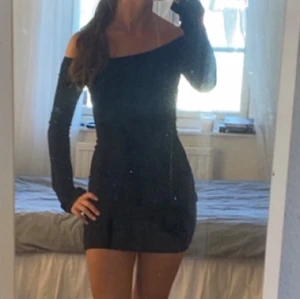 Svart offshoulder kortklänning - Snygg svart kortklänning med offshoulder och långa ärmar. Klänningen har en tight passform som framhäver figuren och är perfekt för dig som gillar en stilren och trendig look.