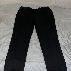 Svarta kostymbyxor Dressmann slim fit - Svarta kostymbyxor från Dressmann i slim fit-modell. Byxorna har bälteshällor, knapp och dragkedja fram. Materialet är en mix av polyester, ull och elastan för en skön och följsam känsla. Perfekta för en clean och stilren look.