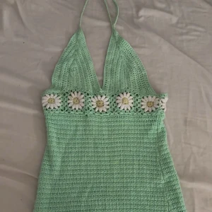 Mintgrön virkad klänning Bershka XS - Superfin mintgrön virkad kortklänning från Bershka med halterneck och virkade blommor i vitt och gult under bysten. Perfekt för sommarens varma dagar och ger en riktigt söt och bohemisk vibe.