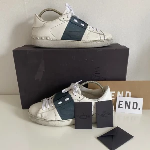 Valentino Garavani Open sneakers vit/grön - Snygga Valentino Garavani Open sneakers i vitt skinn med grön mittpanel och vita snören. Klassisk rund tå, platt sula med nitar baktill och diskret logga på sulan. Perfekta för dig som gillar exklusiva och trendiga sneakers. De är köpt från endclothing och de är 100% äkta