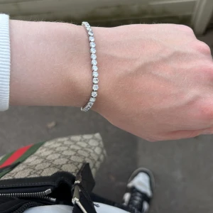 Glittrigt tennisarmband i silverfärg - Snyggt tennisarmband med runda, gnistrande stenar i rad längs hela armbandet. Armbandet är silverfärgat och har en klassisk, elegant design som verkligen fångar ljuset. Perfekt för dig som vill ha något stilrent men ändå extra.