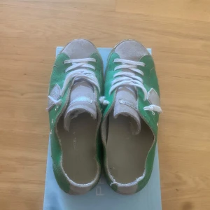 Gröna Philippe Model sneakers i skinn - Snygga gröna sneakers från Philippe Model med vita detaljer och silverfärgad sköld på sidan. Skorna har vit snörning, rund tå och platt sula. Det står även ”phillipe model” under skon. Ovandelen är i skinn och mocka, vilket ger en cool kontrast. Perfekta för dig som vill sticka ut med en unik färg på fötterna. OBS! Pris kan diskuteras!