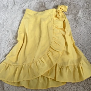 Gul kjol med volang från Lindex - Superfin gul omlottkjol från Lindex med volangkant och knyt i midjan. Den passar mig som har XS. Kjolen har ett tyg på insidan, så den är inte genomskinlig!