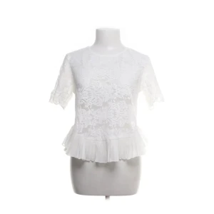 Vit spetsblus med volang - Superfin vit blus i spets med korta ärmar och rund hals. Blusen har ett romantiskt blommönster och avslutas med en söt volangkant nedtill. Perfekt för dig som gillar en feminin och trendig look. Storlek L men lite liten i storleken enligt mig❤️