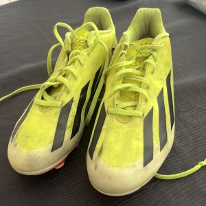 Gula Adidas fotbollsskor med dobbar - Snygga fotbollsskor från Adidas i neon-gult med svarta ränder på sidorna och röda dobbar.            Frakten ingår i priset!