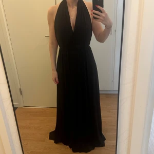 Svart långklänning - Klänningen har omlottliv och kan stylas på många olika sätt upptill. Mjuk och följsam passform, perfekt för en elegant look