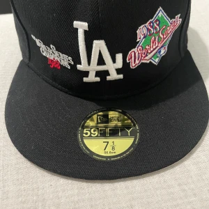 LA Dodgers 59FIFTY keps World Series - Svart LA Dodgers 59FIFTY keps från New Era med broderade loggor, inklusive 1988 World Series patch och MLB-logga bak. Klassisk flat peak och broderad LA framtill. Tillverkad i 100% polyester. Perfekt för dig som gillar sportig streetstyle.
