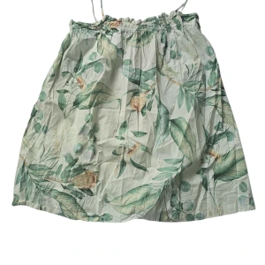 Blommig kortkjol från H&M - Superfin kortkjol från H&M med blommigt mönster i grönt och beige på vit botten. Kjolen har resår i midjan och är gjord i tunn bomull, perfekt för varma dagar. Snygg att matcha med en enkel topp och sneakers.