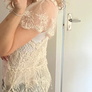 Beige spetsväst med pärlor - Beige väst i spets med blommiga broderier och pärlor på ärmarna. Står ej storlek eller märke men sitter som XS/S