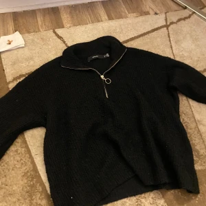 Svart stickad half zip-tröja Vero Moda - Svart stickad tröja från Vero Moda med hög krage och snygg half zip-dragkedja med ringdetalj. Långärmad och i en lite loose passform, perfekt för lager-på-lager. Mjuk och mysig känsla, passar till allt.