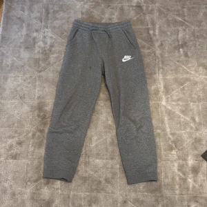 Grå mjukisbyxor från Nike - Säljer ett par grå mjukisbyxor från Nike med elastisk midja och snörning. Byxorna har två sidofickor och en liten Nike-logga på vänster ben. Perfekta för en avslappnad stil eller träning.