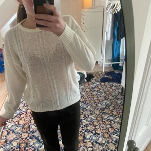 Vit stickad tröja - Säljer en vit stickad tröja med ett diskret mönster. Tröjan har långa ärmar och en rund halsringning. 