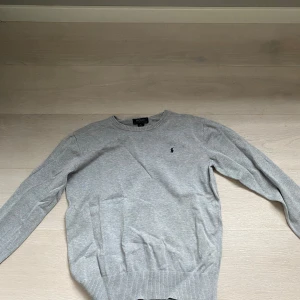 Grå tröja från Ralph Lauren xs/s - Säljer en stilren grå tröja från Ralph Lauren med deras ikoniska logga broderad på bröstet. Tröjan har långa ärmar och ribbade muddar vid ärmslut och nederkant. Perfekt för en avslappnad och snygg look. (Pris kan diskuteras)