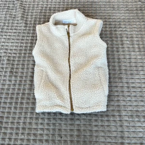 Vit fleeceväst från H&M - Mysig vit fleeceväst från H&M med dragkedja framtill. Perfekt för kyliga dagar och enkel att matcha med andra plagg. Västen har en klassisk design med två fickor på sidorna.