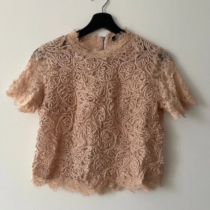 Beige spetsblus från Zara  - Säljer en elegant beige spetsblus från Zara. Blusen har korta ärmar och en dragkedja i ryggen. Perfekt för en stilren look med vackra spetsdetaljer. Den är lite liten i stl, kanske mer åt stl S