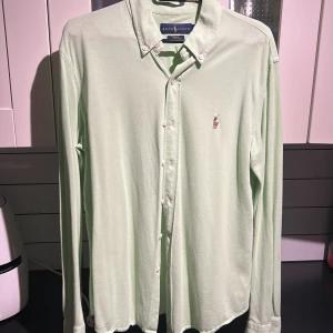 Grön skjorta från Ralph Lauren - Snygg ljusgrön skjorta från Ralph Lauren i slim fit. Skjortan har långa ärmar och klassisk krage med knappar. Den är broderad med den ikoniska logotypen på bröstet.