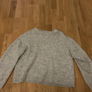 Grå stickad tröja - Säljer en stilren grå stickad tröja med normal passform. Tröjan har långa ärmar och en rund halsringning, perfekt för kyligare dagar. Enkel och tidlös design som passar till det mesta.