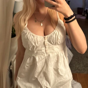 Vitt linne - Säljer en söt vitt linne med knappar framtill och smala axelband. Linnet har en lätt rynkad design vid bysten och en luftig passform, perfekt för varma dagar.storlek one size