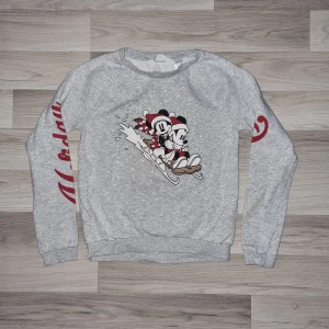 Grå tröja med Disney-motiv från H&M - Säljer en grå långärmad tröja från H&M med ett gulligt Disney-motiv på framsidan. Tröjan har texten 'Dreams' i rött på ärmarna. Perfekt för alla Disney-fans! 💫