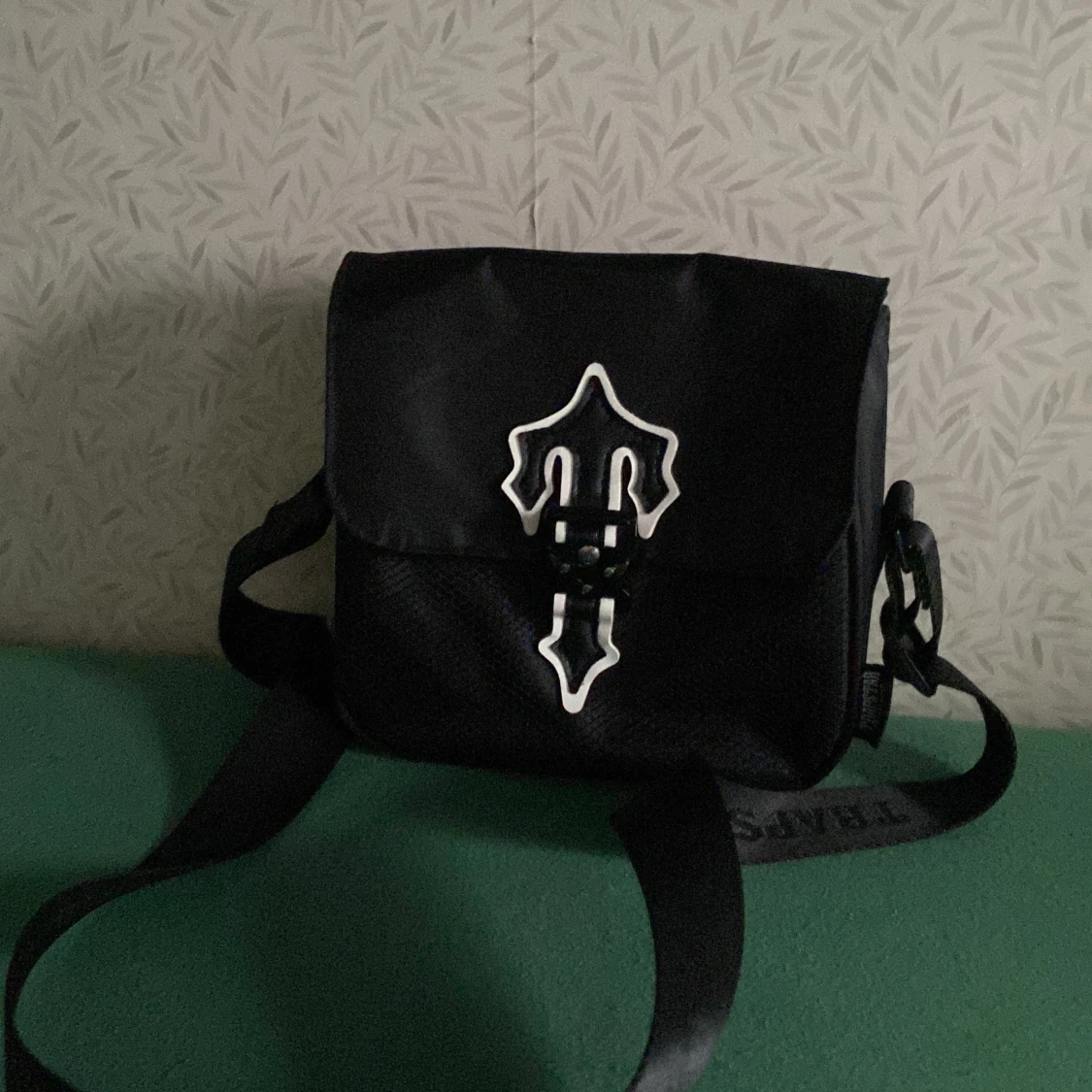 Svart axelväska med dekorativt emblem