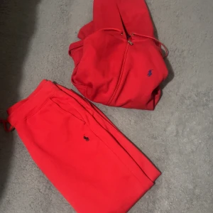 Polo tracksuit  - Säljer en snygg röd hoodie från Polo Ralph Lauren med dragkedja och justerbar huva. Den har en liten blå logga på bröstet. Perfekt för en avslappnad stil.