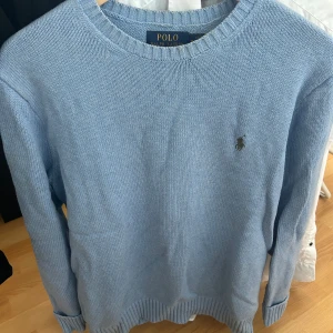 Ljusblå stickad tröja från Ralph Lauren - Säljer en stilren ljusblå stickad tröja från Ralph Lauren. Tröjan har en rund halsringning och ett diskret broderat märke på bröstet. Perfekt för en avslappnad men elegant look.