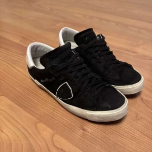 Svarta sneakers från Philippe Model - Snygga svarta sneakers från Philippe Model i mocka med vita detaljer. Skorna har en klassisk design med snörning och en bekväm sula. Perfekta för en stilren look. Finns även autentisk tagg så de är äkta. Snabb affär prioriteras och pris kan även diskuteras något. 