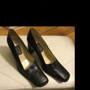 Svarta pumps från Tiger - Snygga svarta pumps från Tiger med fyrkantig tå och klack. Perfekta för en stilren look. Tillverkade i skinn för en elegant finish.